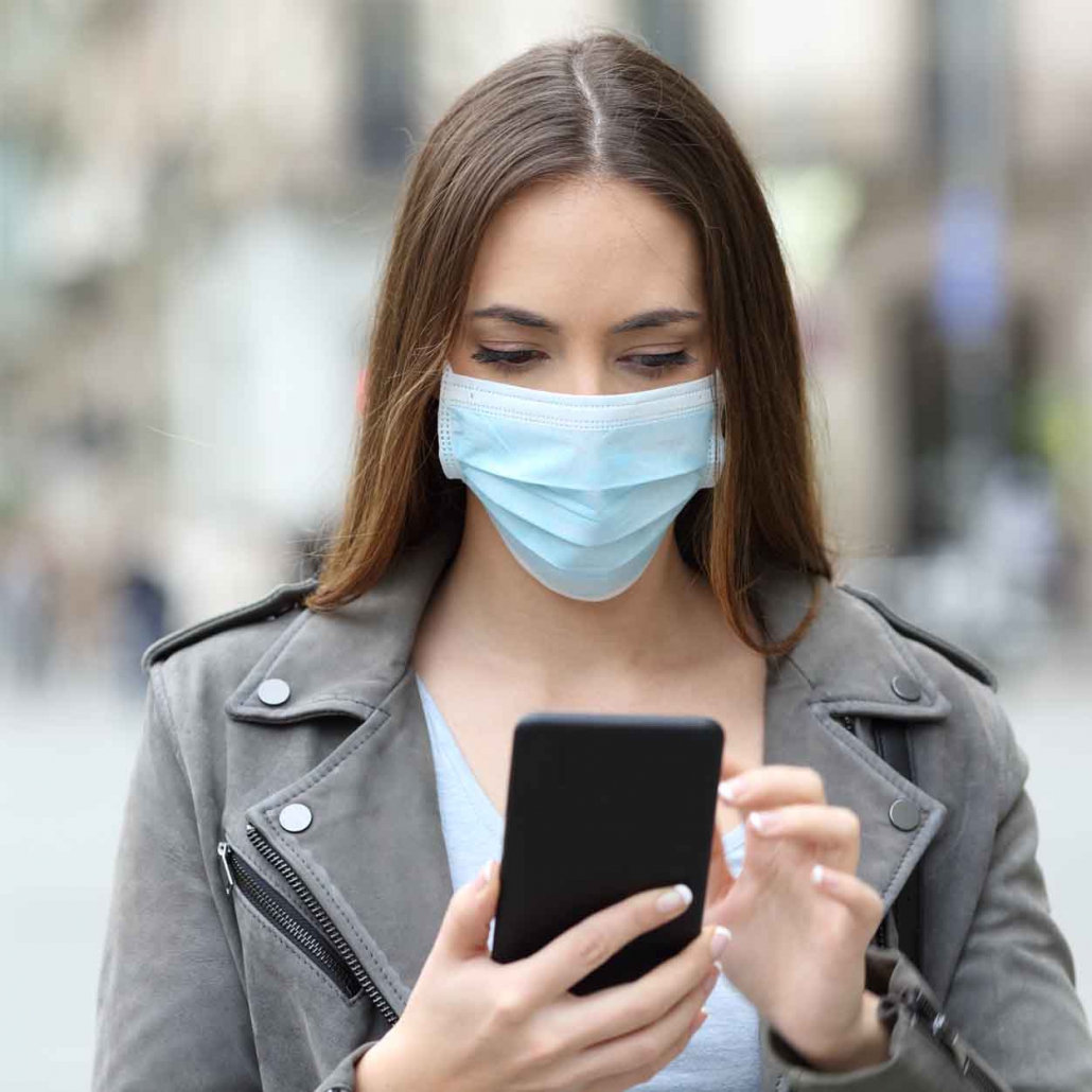 Serious girl with mask checking her phone on street
